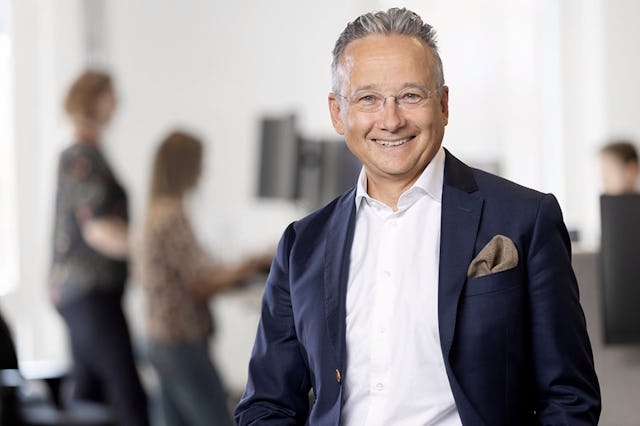 Joachim Hallengren i kostym i förgrunden, med suddiga individer i bakgrunden.