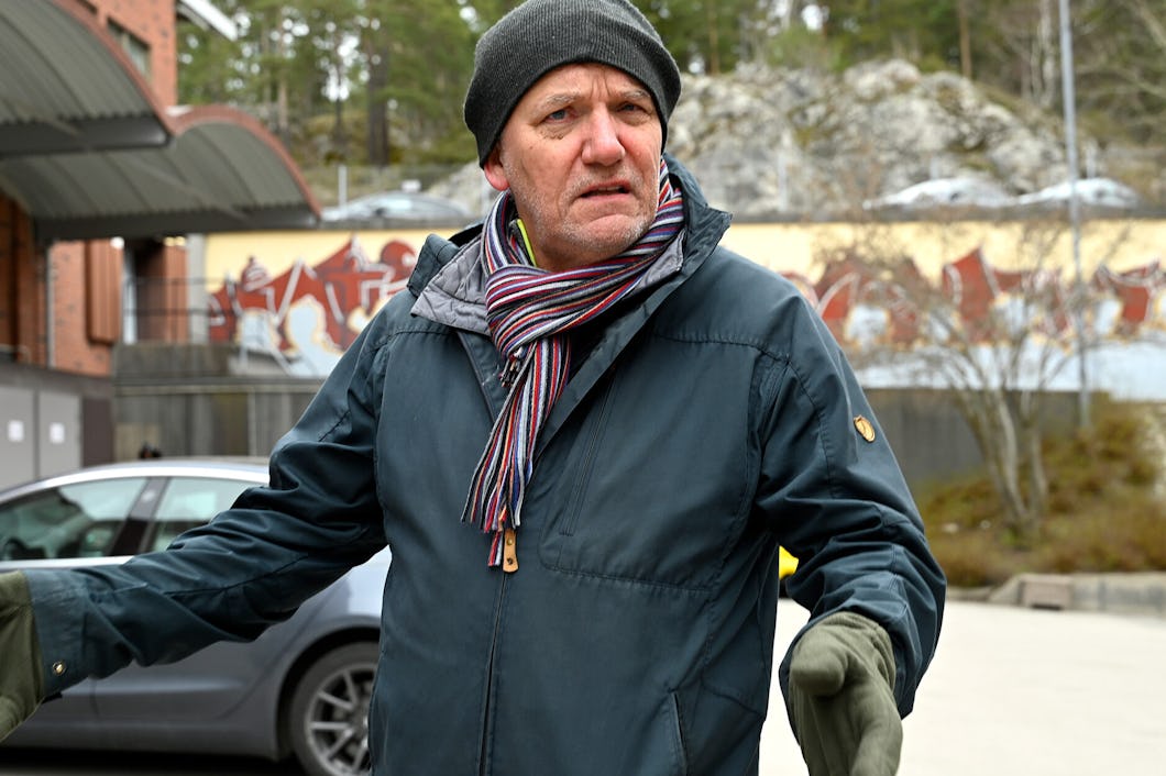 En man i vinterrock, halsduk och handskar står utomhus.