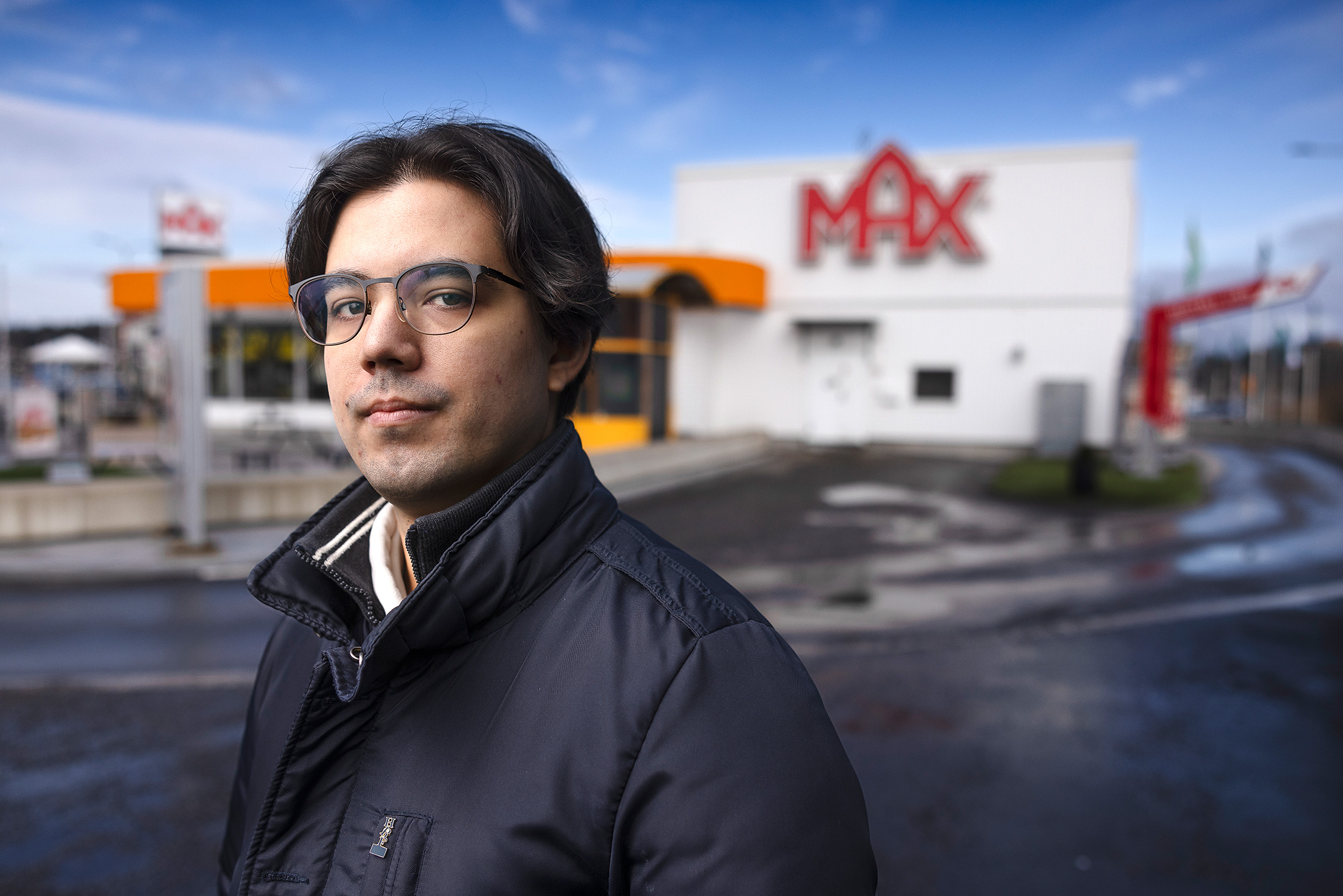 Skyddsombudet Kim Franzén står framför en Max snabbmatsrestaurang under molnfylld himmel.