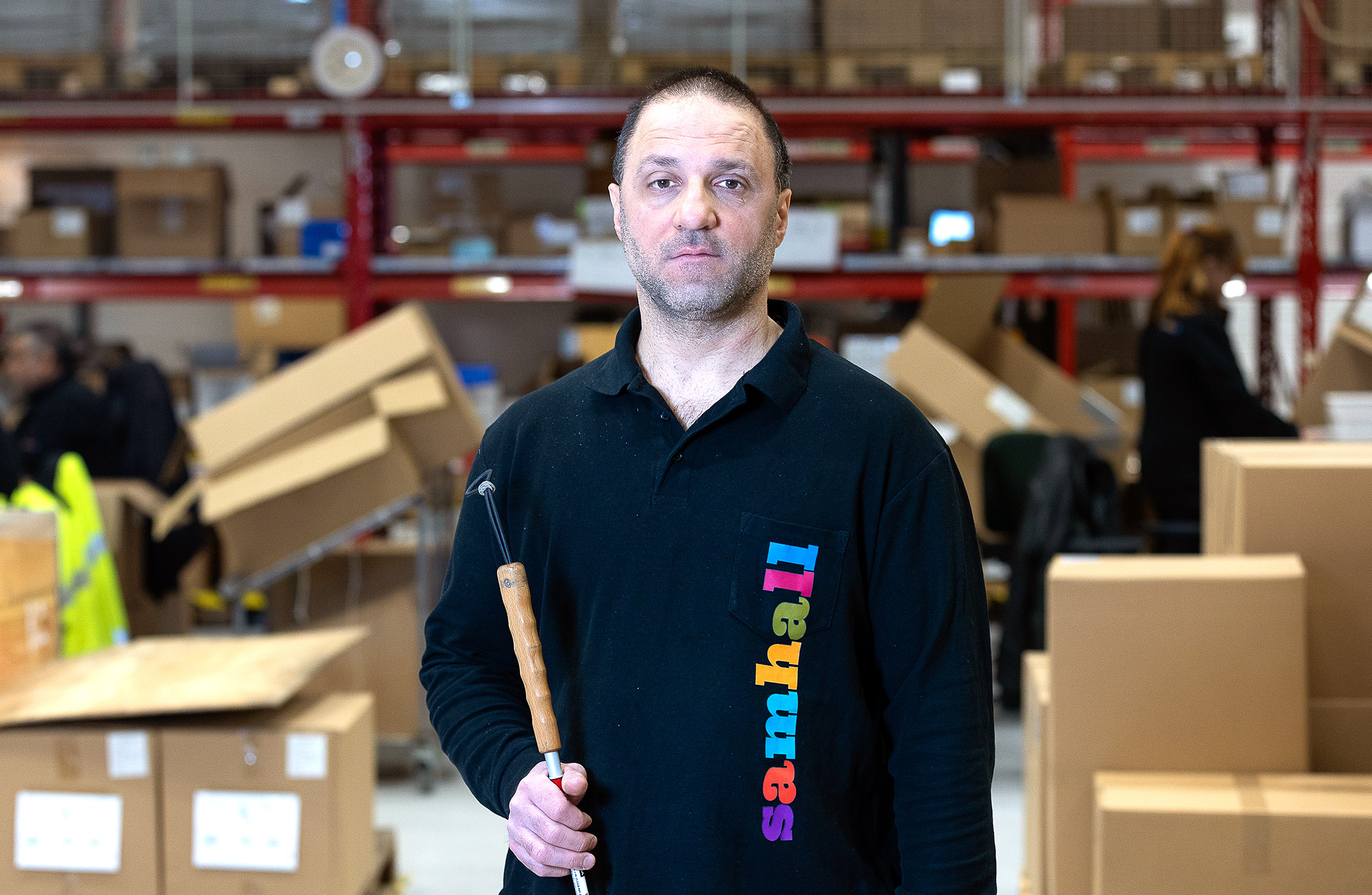 Saddik som håller i ett verktyg står i ett lager med lådor i bakgrunden.