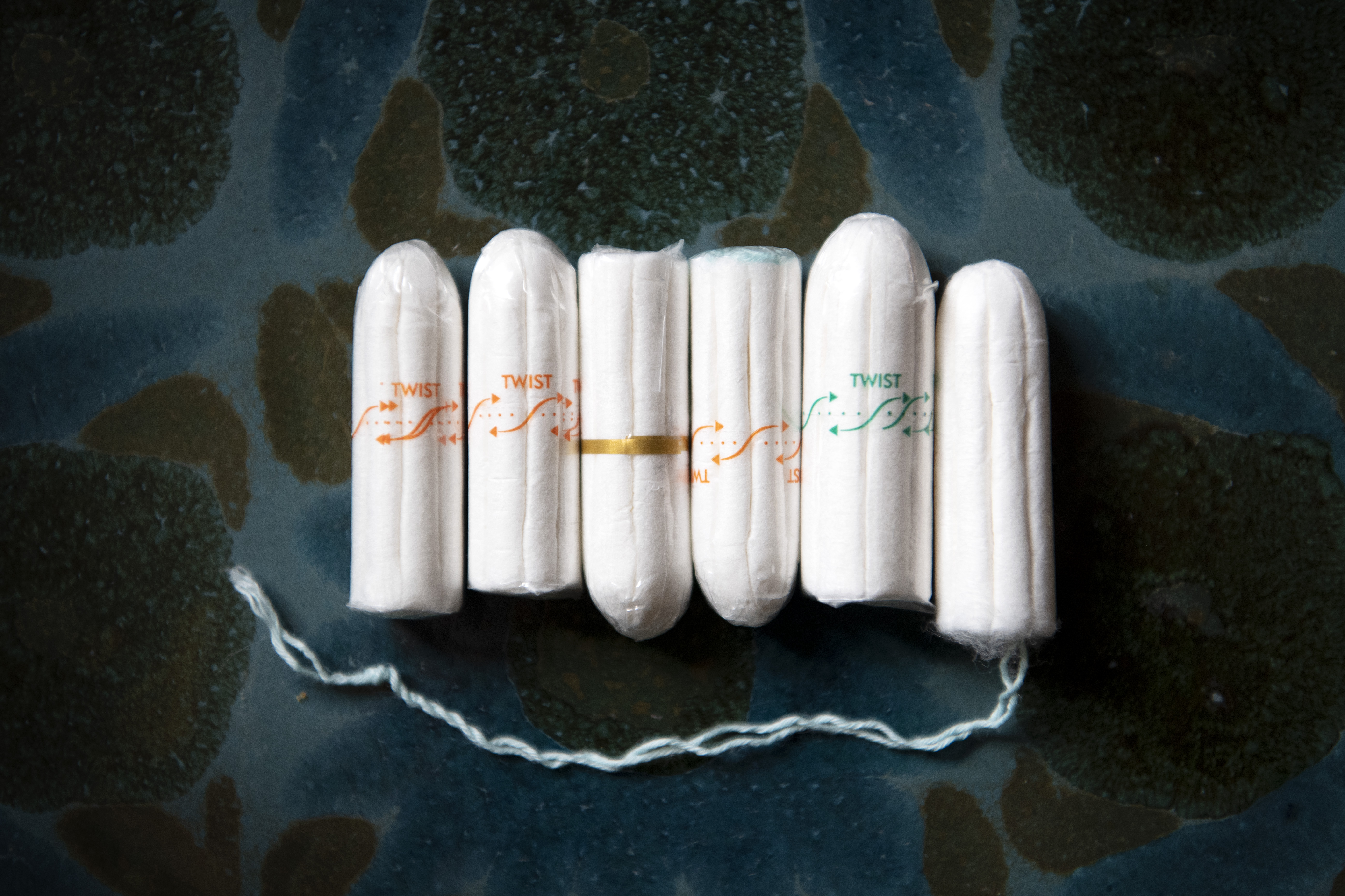 Applikatorförsedda tamponger, nio stycken, ordnade i rad på en melerad blå bakgrund.