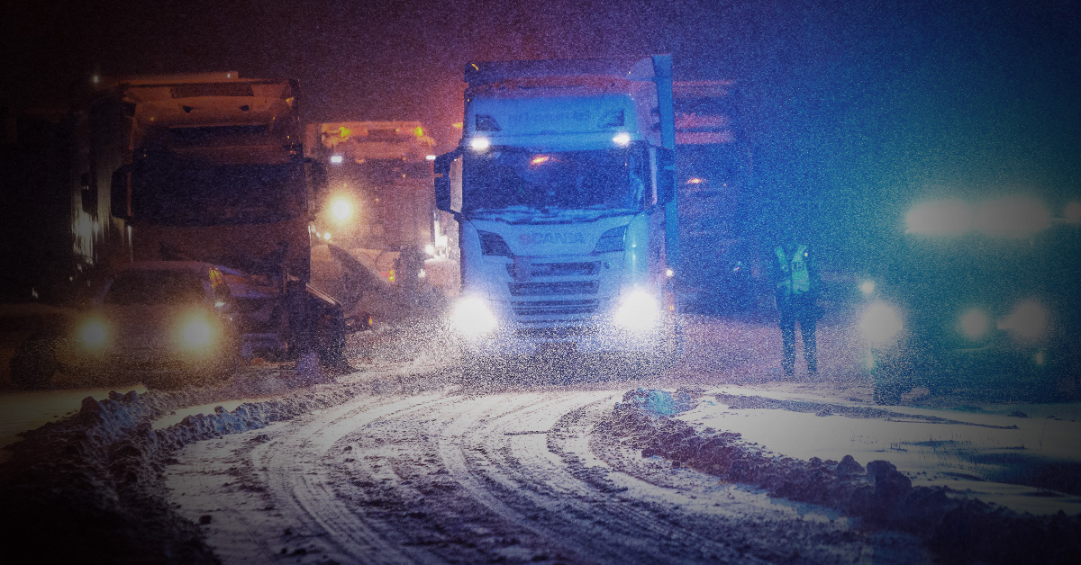 Fordon som navigerar en snötäckt väg på natten med nedsatt sikt.