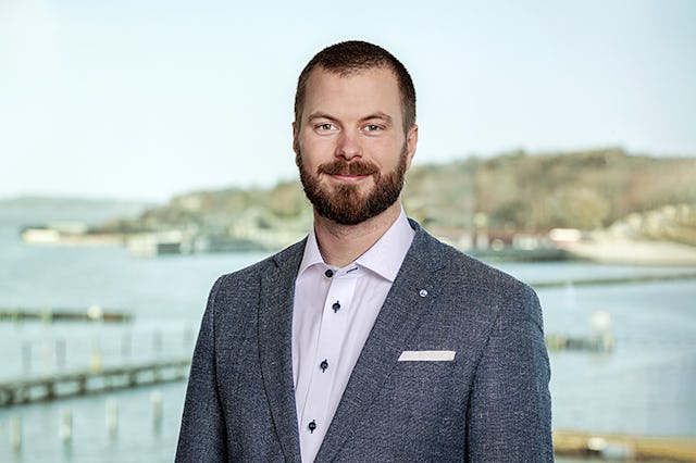 Jonatan Höglund i kostym med bryggor och byggnader i bakgrunden.