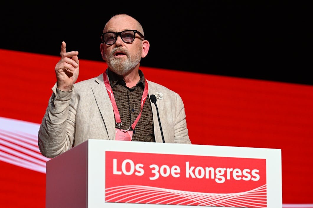Johan Lindholm med glasögon och kavaj talar vid ett podium framför en röd bakgrund som visar texten "LOs 30e kongress" i vitt.