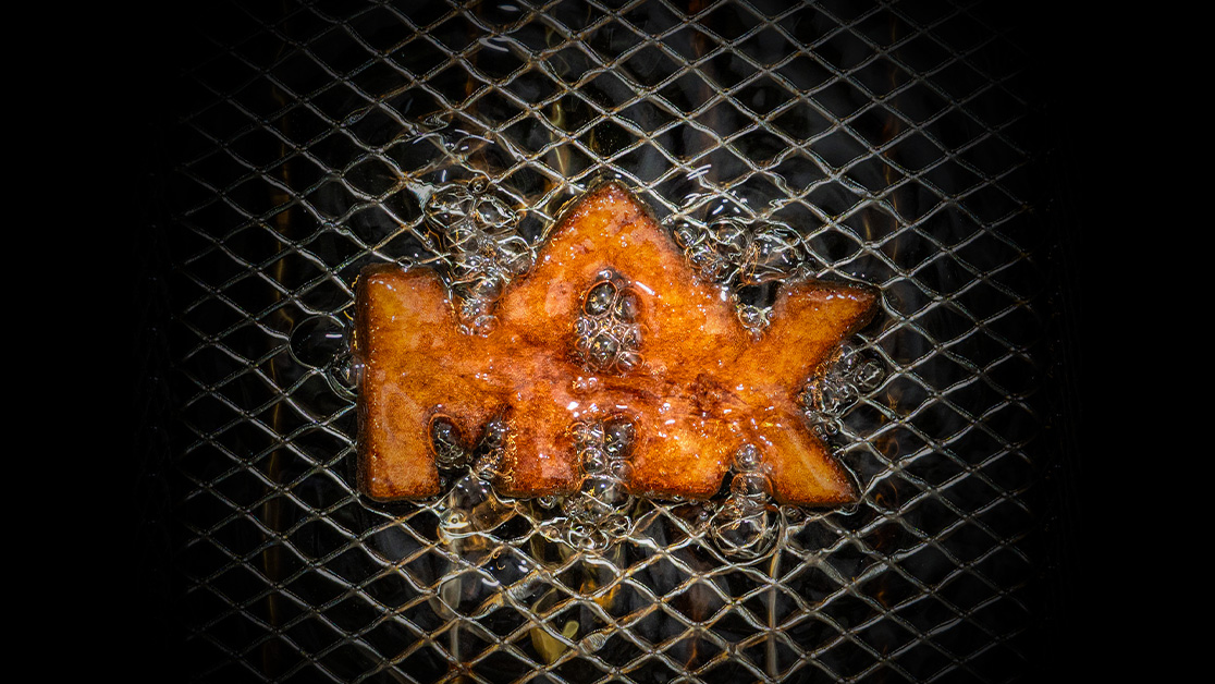 Max-logga gjord av potatis omgivet av oljebubblor, friteras.