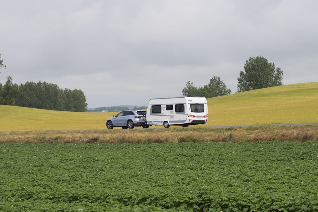Ett fordon som drar en husvagn som rör sig på en väg med omgivande fält och en mulen himmel.
