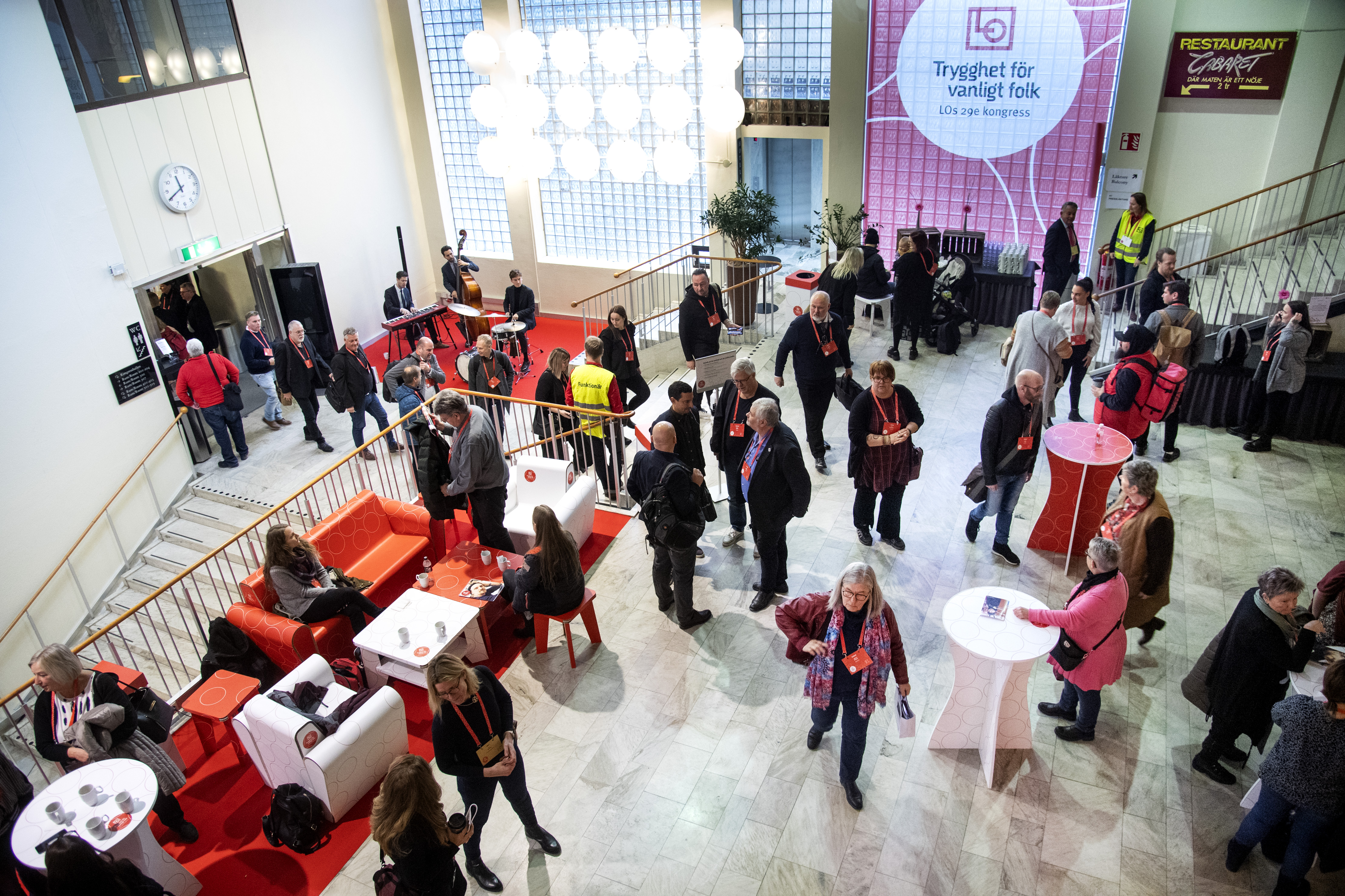 Individer som interagerar och rör sig i en stor lobby med en trappa.