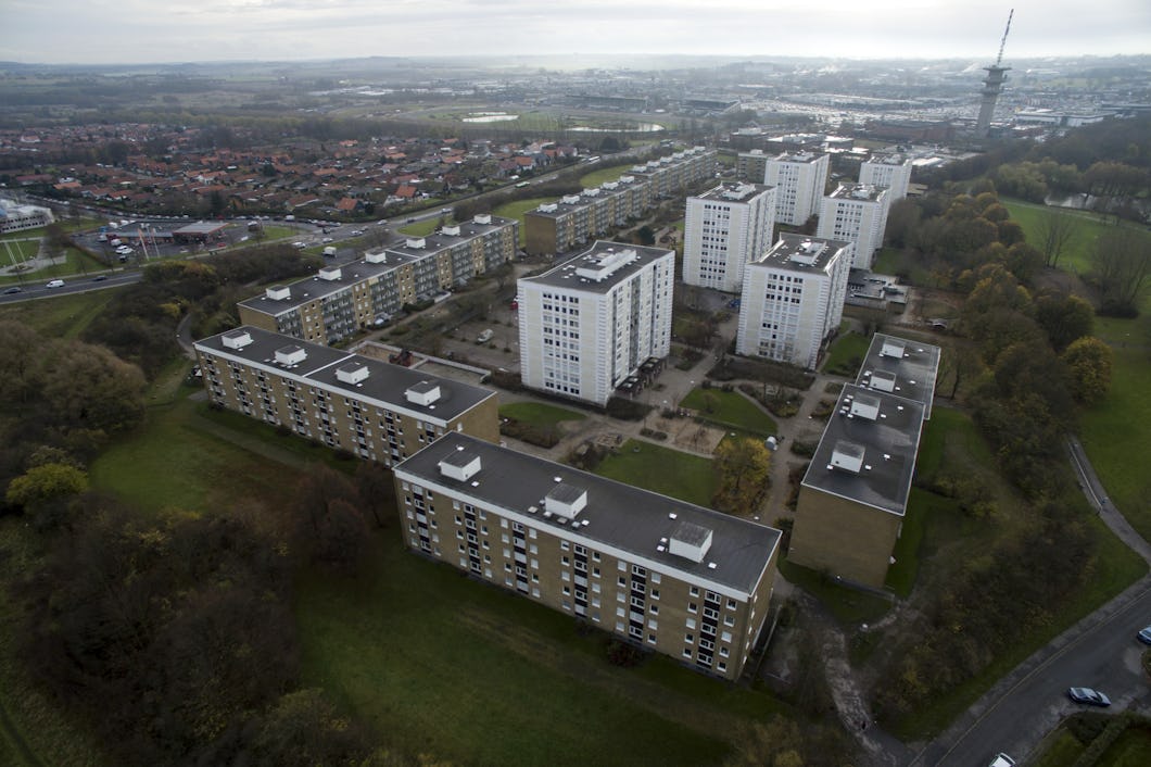 Bild på ett bostadsområde sett från ovan med flera höghus omgivna av grönområden och vägar, under en molntäckt himmel.