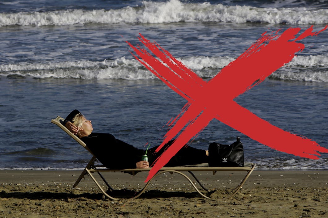 En person i svart klädsel som ligger på en strandstol vid havet, med ett stort rött "X" över bilden.