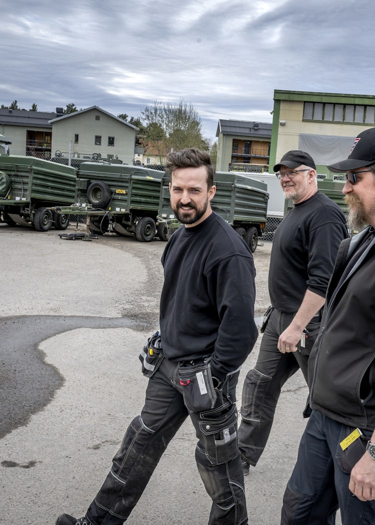 Andreas Grimmesten, Isac Nygren och Kent Persson går utomhus med militärfordon i bakgrunden.