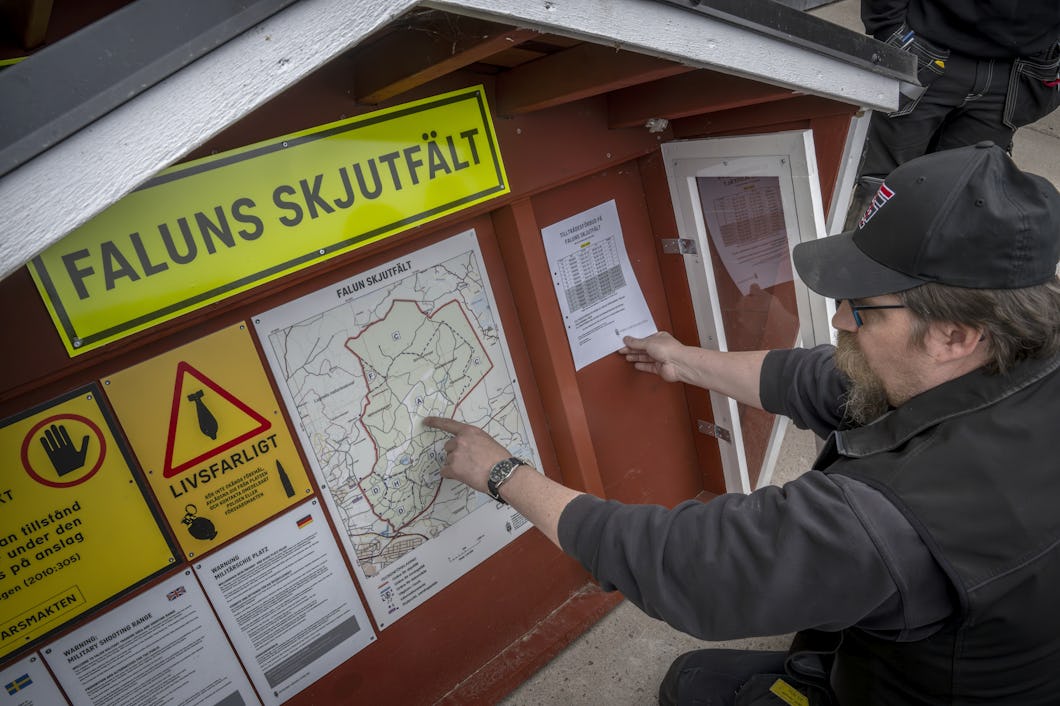 Kent Persson pekar på en karta på en tavla med rubriken "Faluns Skjutfält" samt varningsskyltar och informationsblad.