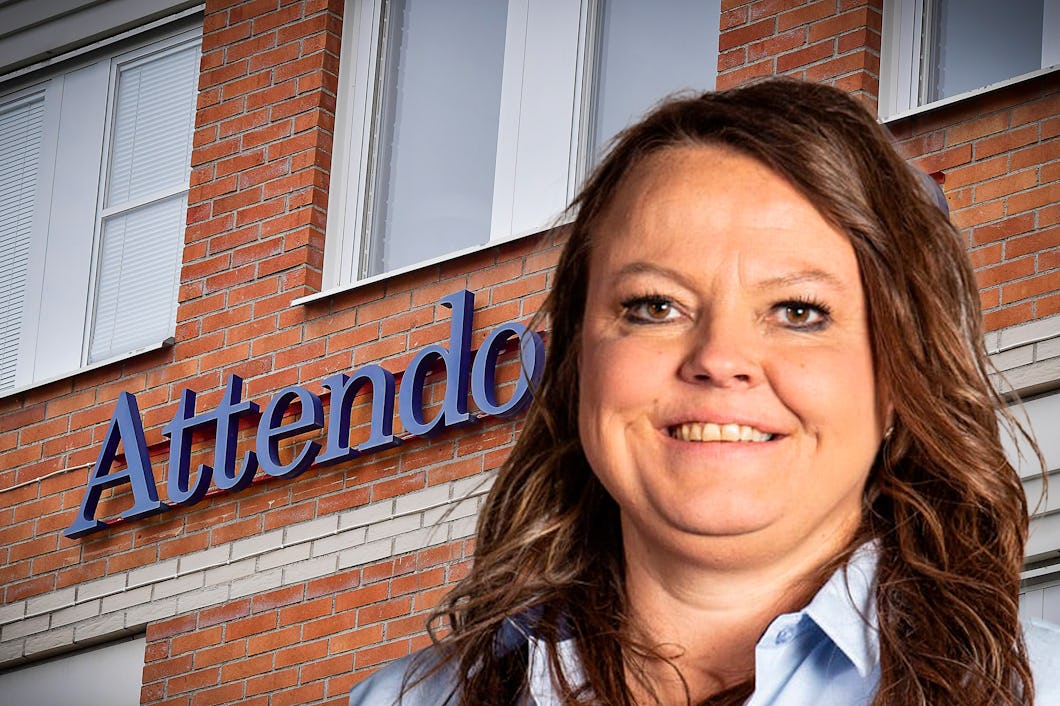 En kvinna med långt hår står framför en tegelbyggnad med skylten "Attendo". Hon ler.