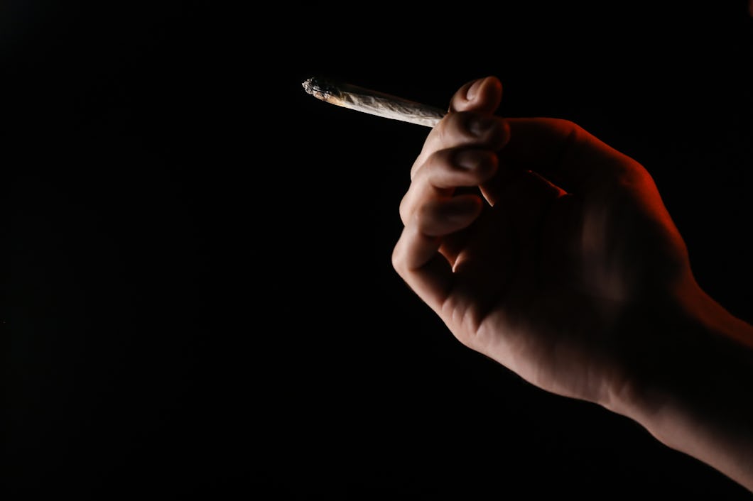 Närbild av en hand som håller en delvis rökt joint mot en mörk bakgrund.