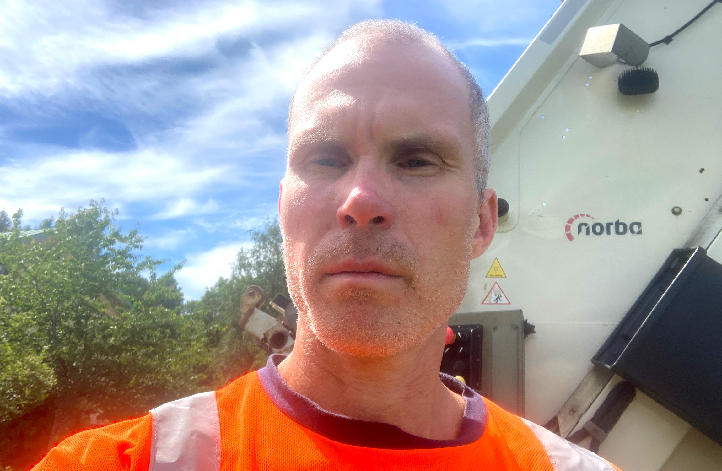 En man i en orange varselväst står framför industriell utrustning.