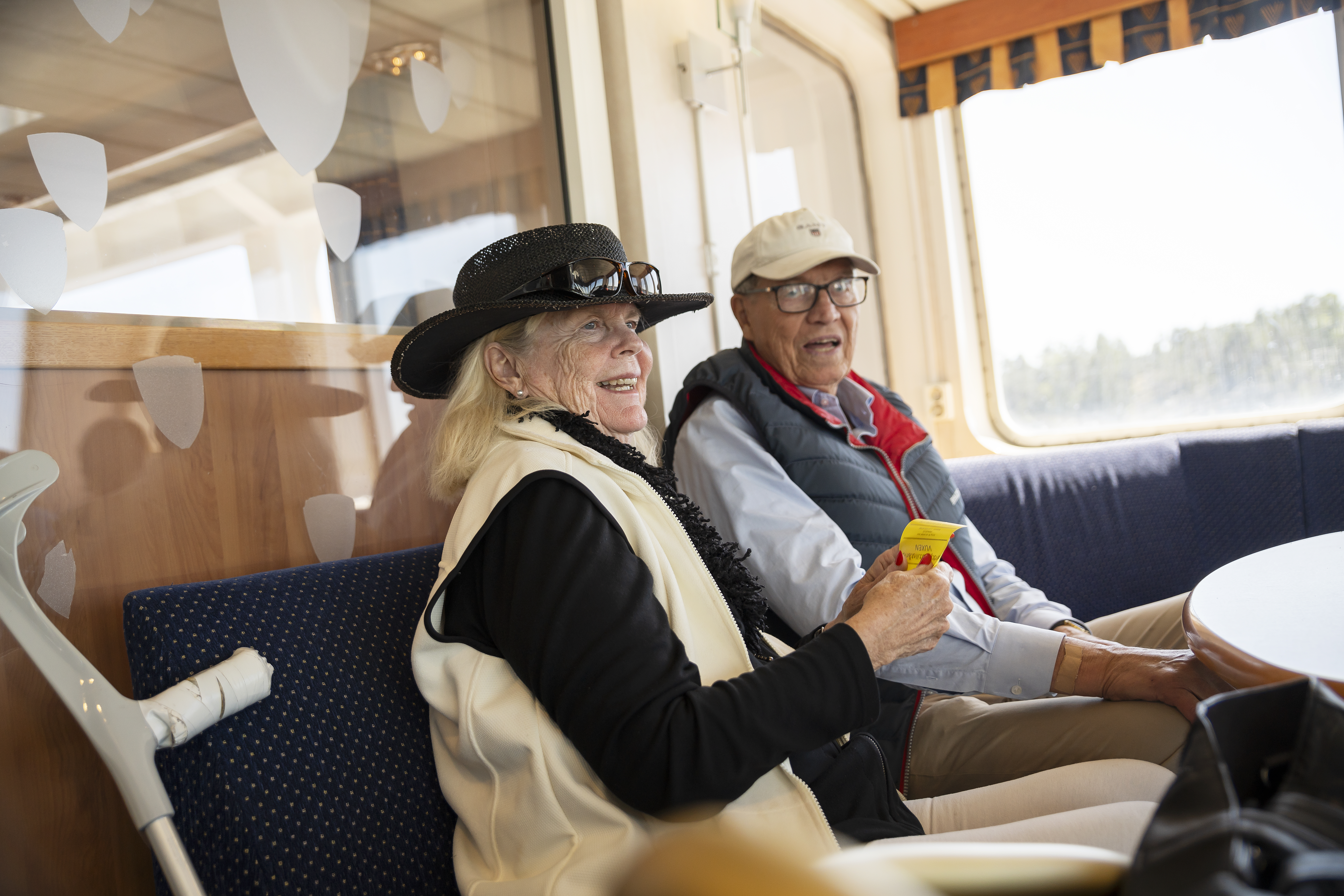 Kvinna med hatt, man med keps ombord på skärgårdsbåt.