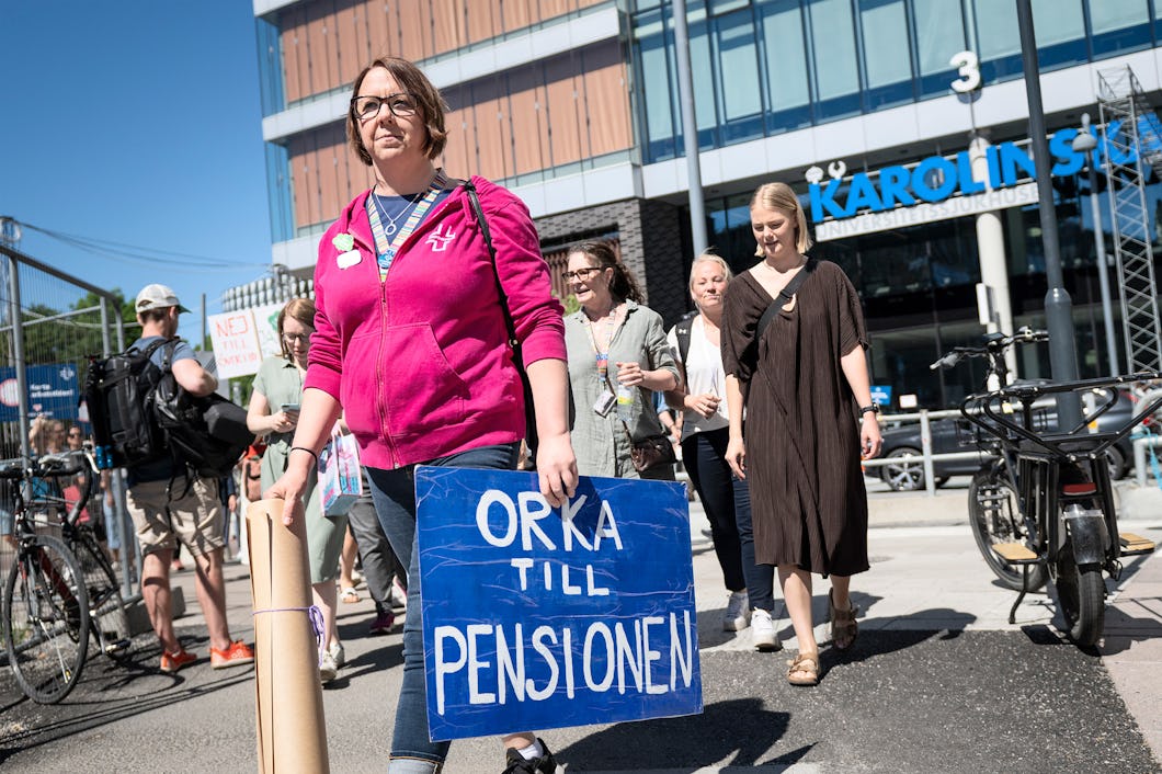 En person i rosa huvtröja håller en blå skylt som lyder "ORKA TILL PENSIONEN".