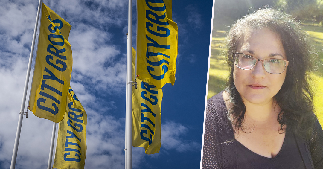 Tre gula flaggor med blå text där det står “CITYGROSS“. Till höger står en person med långt, mörkt hår och glasögon.