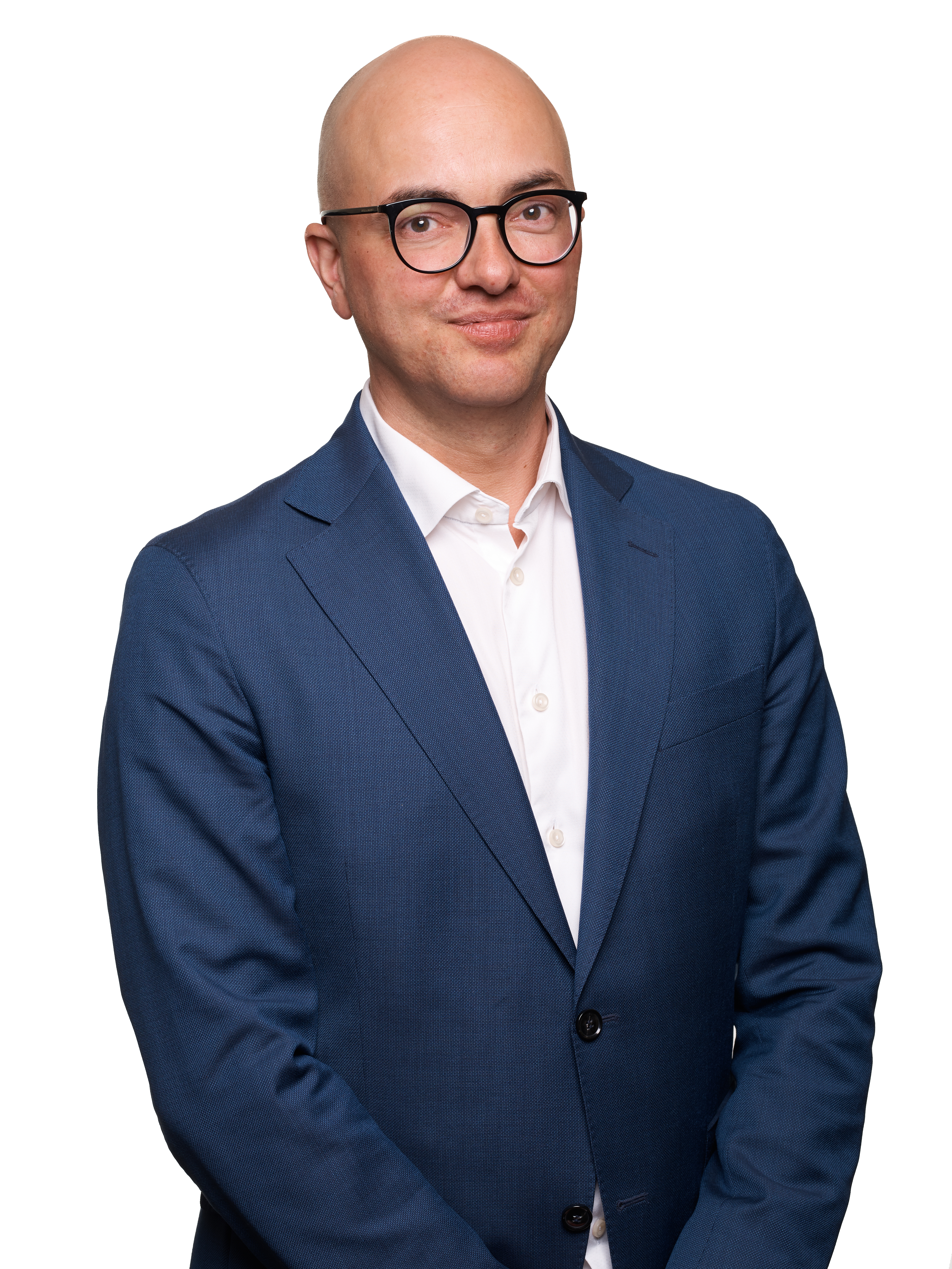 Torbjörn Hållö med glasögon, iklädd en blå kostym och vit skjorta, står mot en vit bakgrund och tittar in i kameran.