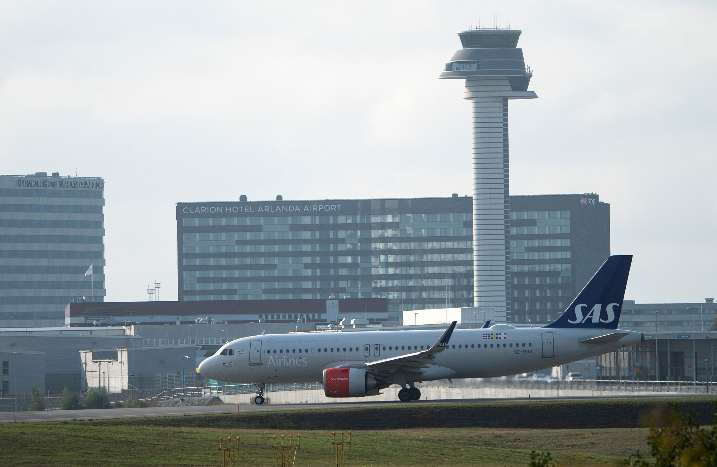 Ett SAS-flygplan står på flygplatsens asfalt med Clarion Hotel Arlanda Airport och en kontrolltorn synliga i bakgrunden.