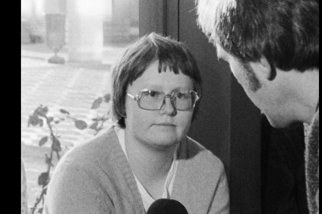 Svartvit arkivbild där Britt-Marie Johansson i gammaldags glasögon intervjuas av en reporter med mikrofon.