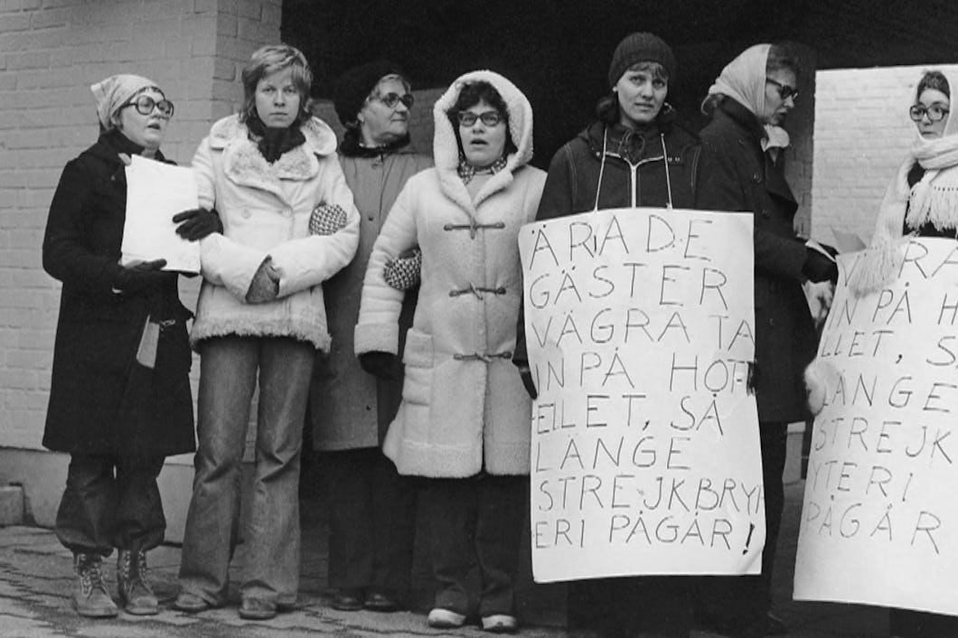 Svartvit arkivbild från 1974 på strejkande städerskor med plakat. På ett av dem står det ”Ärade gäster vägra ta in på hotellet så länge strejkbryteri pågår!”