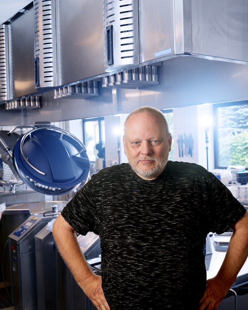 Kaj Jensen står i ett kommersiellt kök med rostfri utrustning och en stor blå koksapparat i bakgrunden.