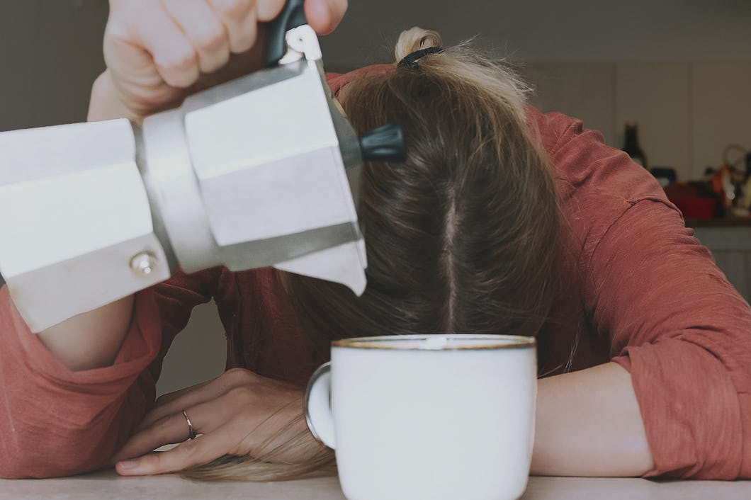 En vilar huvudet mot bordet och häller kaffe från en bryggare i enkopp.