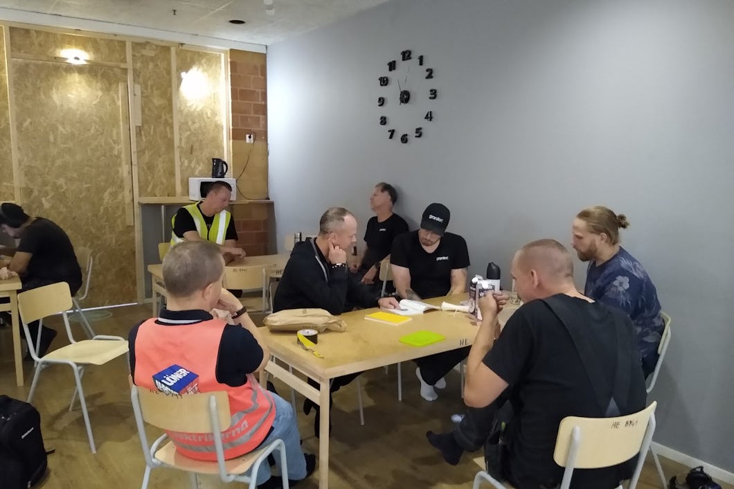 En grupp elektriker sitter runt träbord i ett rum.