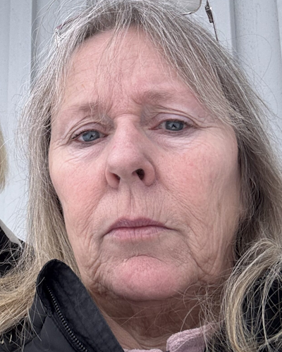 Närbild av Susanne Werdien med långt, ljust hår och glasögon vilande på huvudet. Personen tittar direkt i kameran med ett neutralt ansiktsuttryck.
