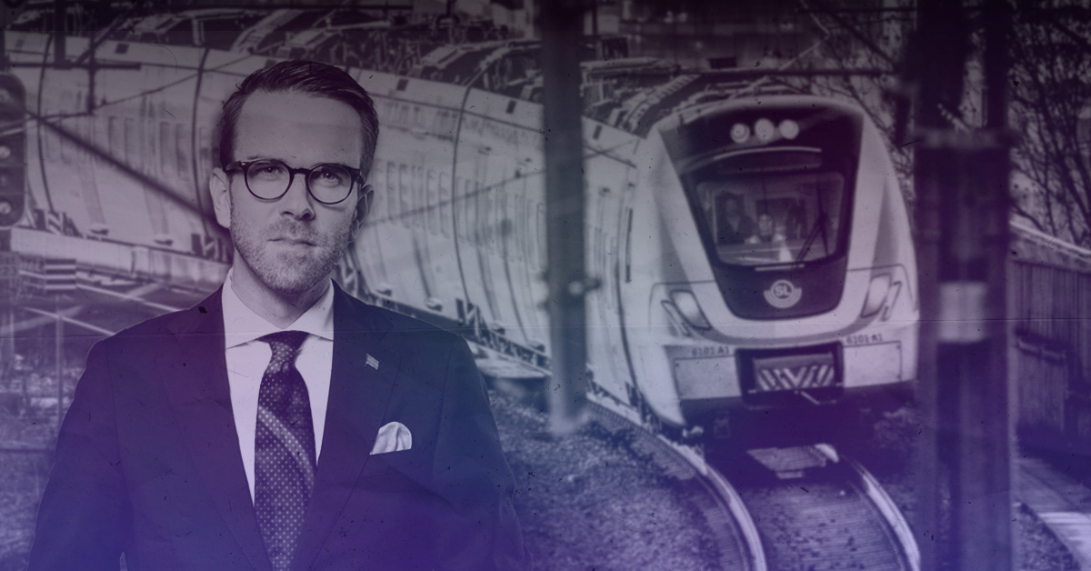 En man i kostym och glasögon står i förgrunden. Bakom honom kör ett pendeltåg på spår. Bilden har en blå-lila ton.