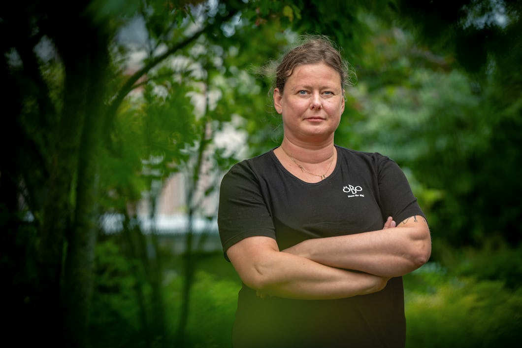 Caroline Håkansson står utomhus med armarna i kors, omgivet av grönska, iförd en svart t-shirt.