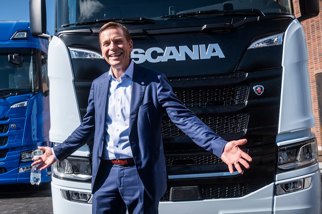 En man i kostym står framför en Scania-lastbil. Han sträcker ut armarna.
