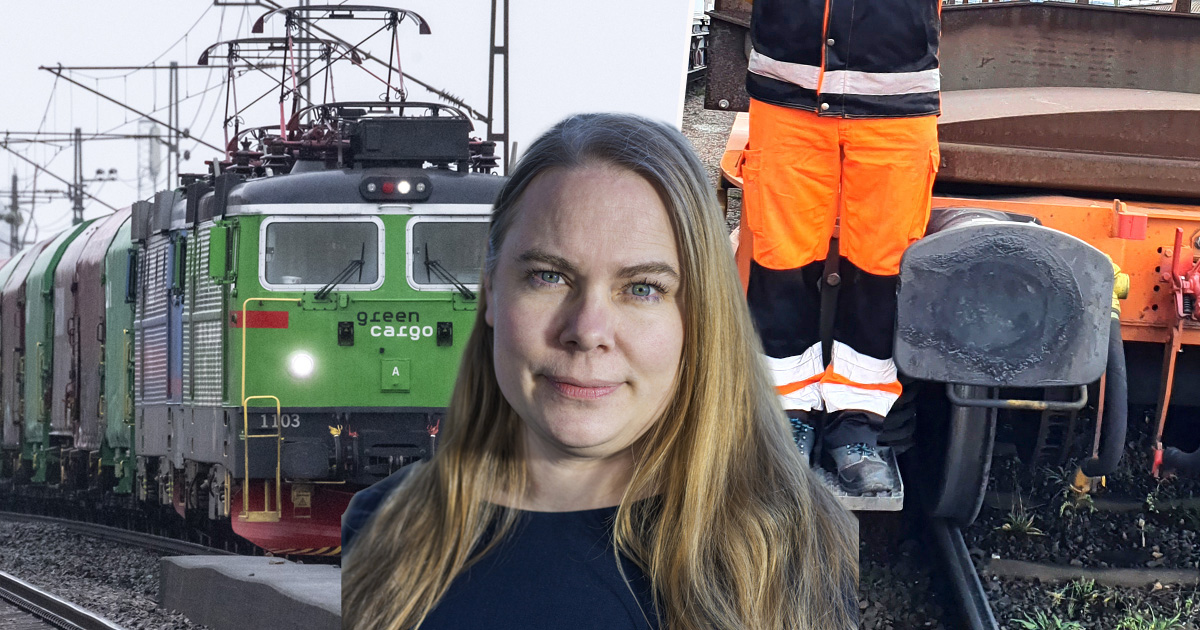 En kvinna med långt blont hår står i förgrunden; bakom henne finns ett grönt godståg och en person i orangea reflekterande arbetskläder nära en järnvägsspår.
