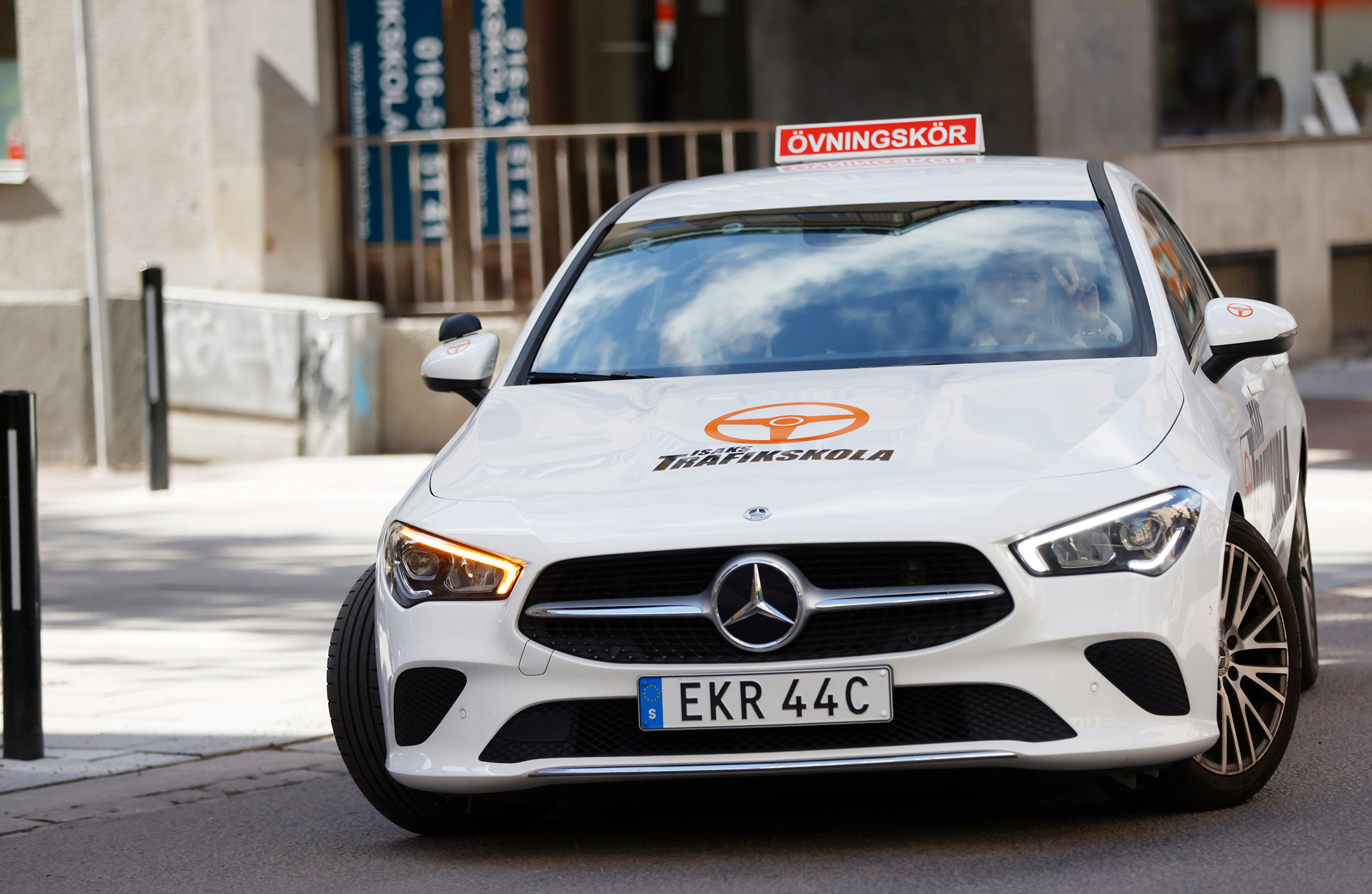En vit Mercedes-Benz med en "Övningskör" skylt på taket.
