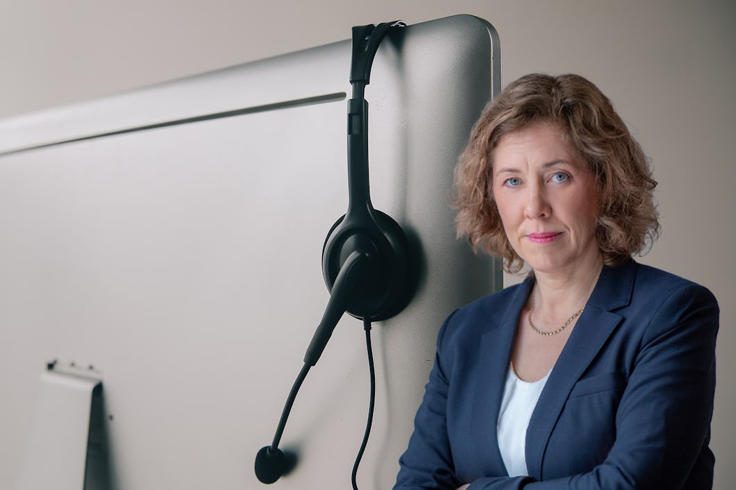 Kvinna i affärskläder står bredvid en datorskärm med ett headset hängande på skärmen.
