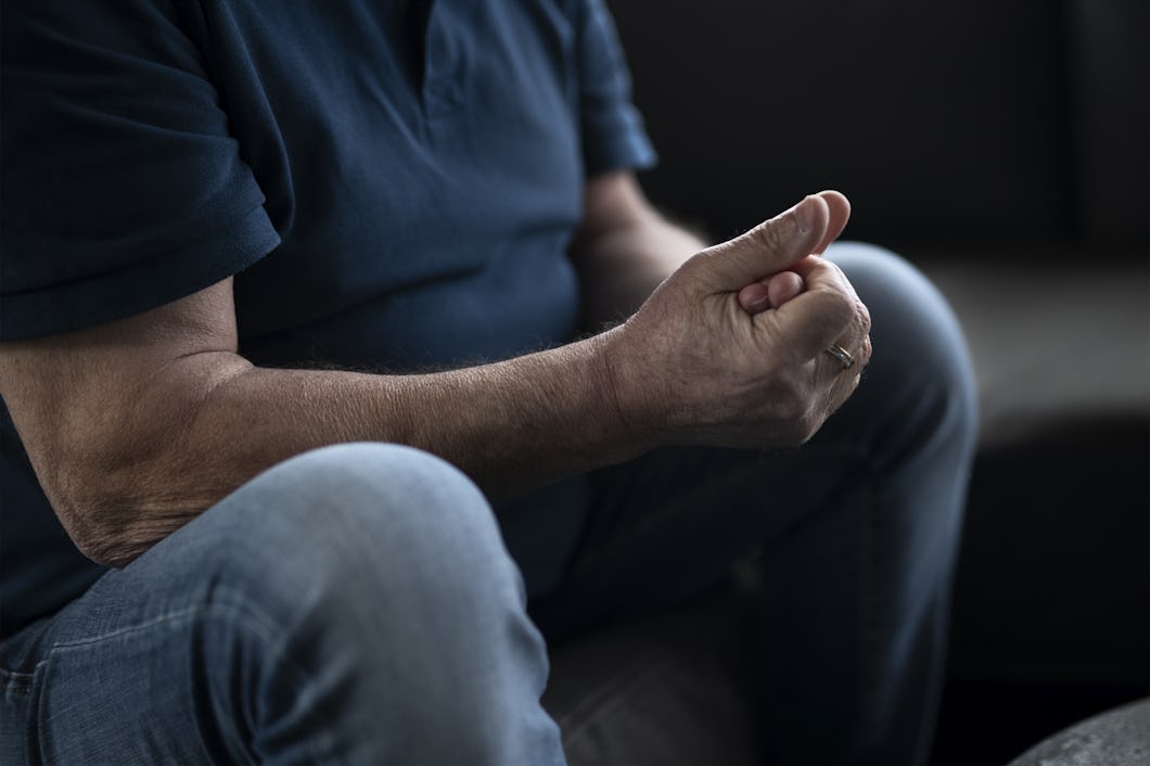 En person sitter med knutna händer, klädd i en mörk tröja och jeans.