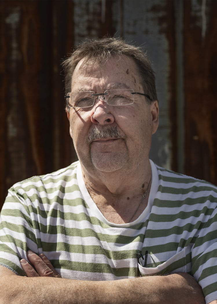 Bengt Sandberg står med armarna i kors framför en väderbiten, rostig metallvägg.
