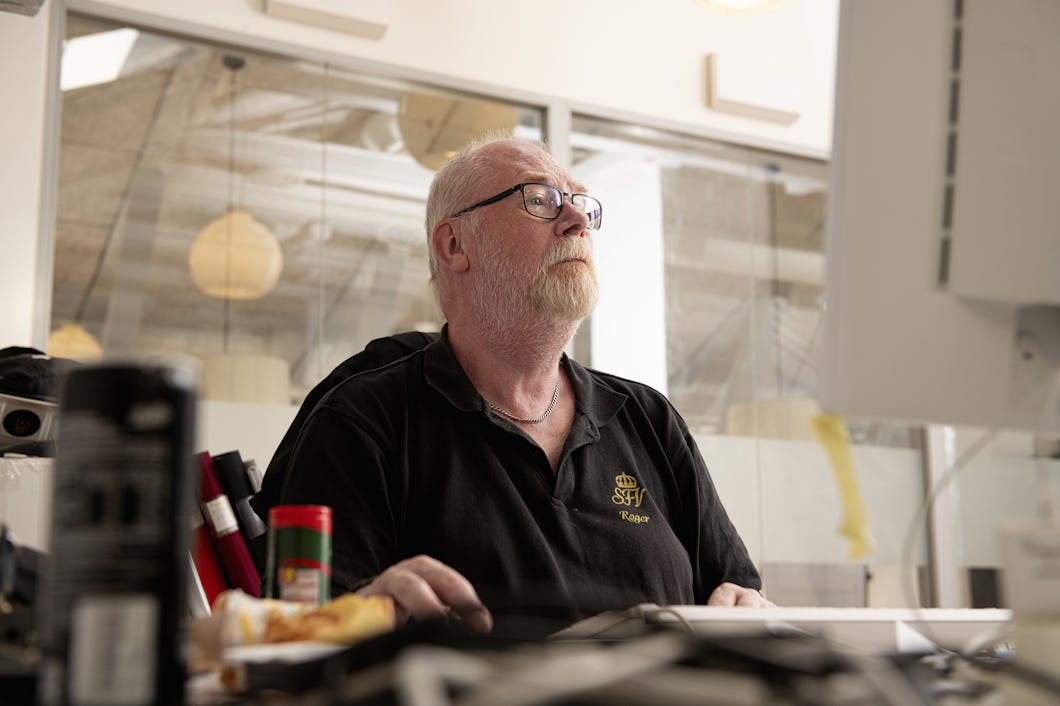 Roger Carlsson sitter vid ett skrivbord och arbetar vid en dator. Kontorsmaterial syns runt honom.