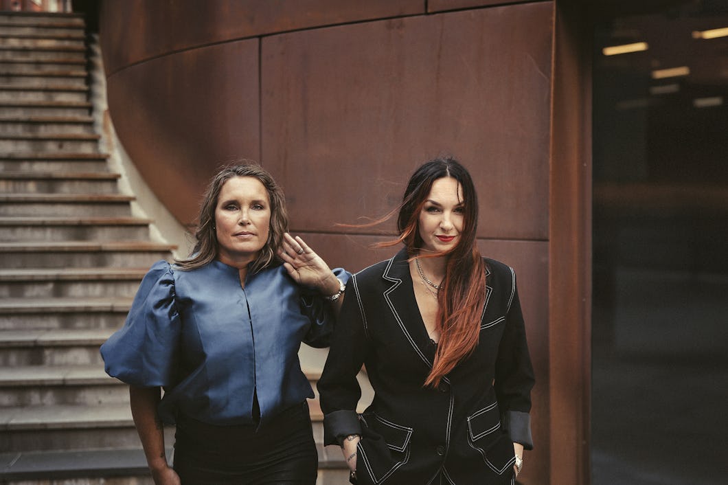 Anna Jinghede och Lena Ljungdahl står tillsammans i en modern byggnad med en böjd trappa.