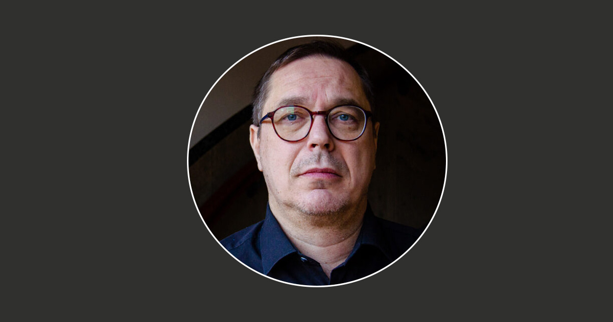 Daniel Lind med glasögon, iförd en mörk skjorta, mot en mörk och något oskarp bakgrund.