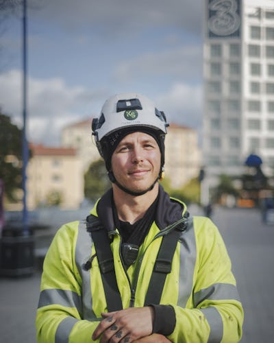 Sebastian Fallman bär en reflekterande gul jacka och hjälm och står utomhus.