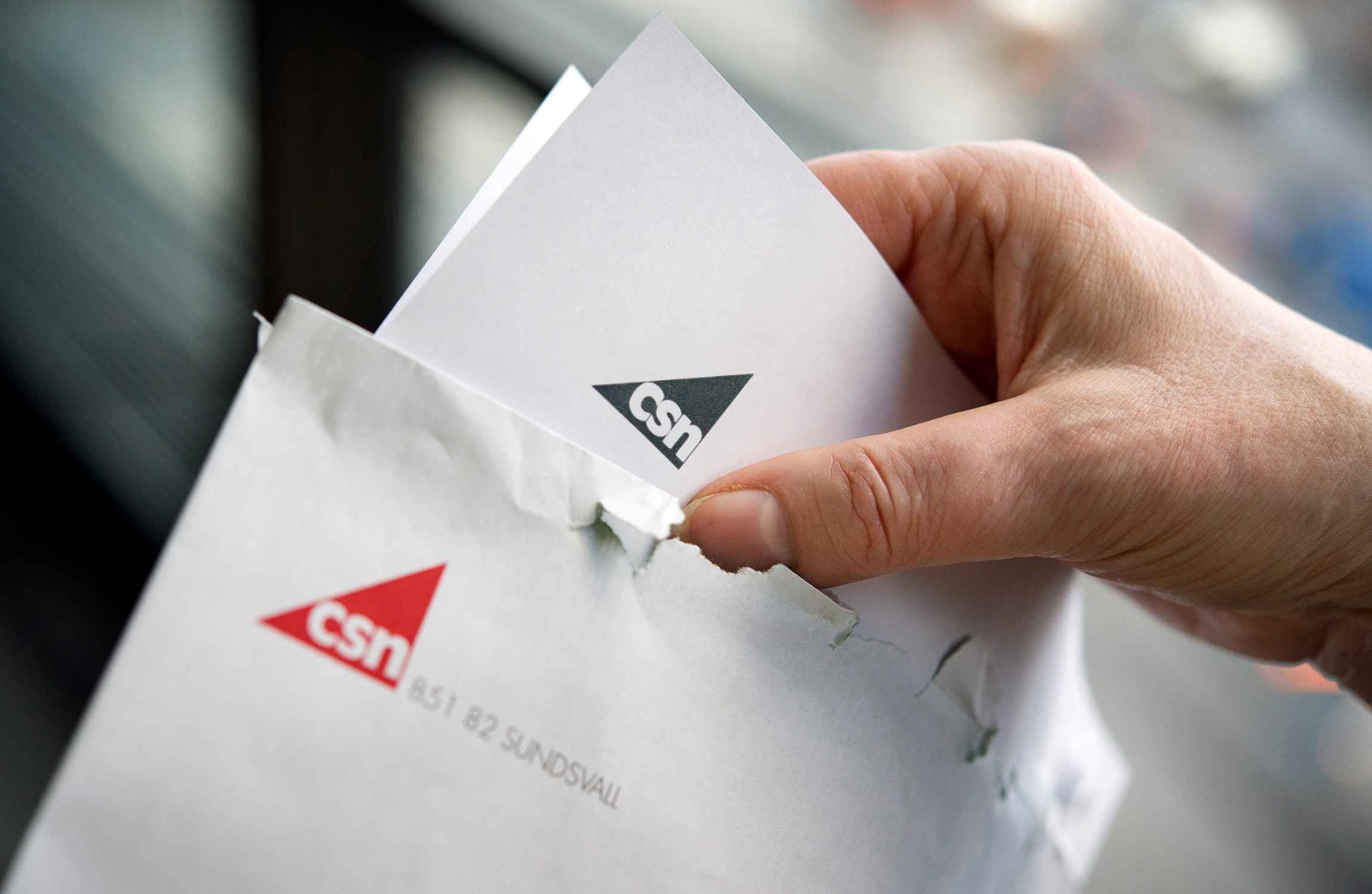 En hand håller ett kuvert och ett brev, båda med logotypen och namnet "CSN.