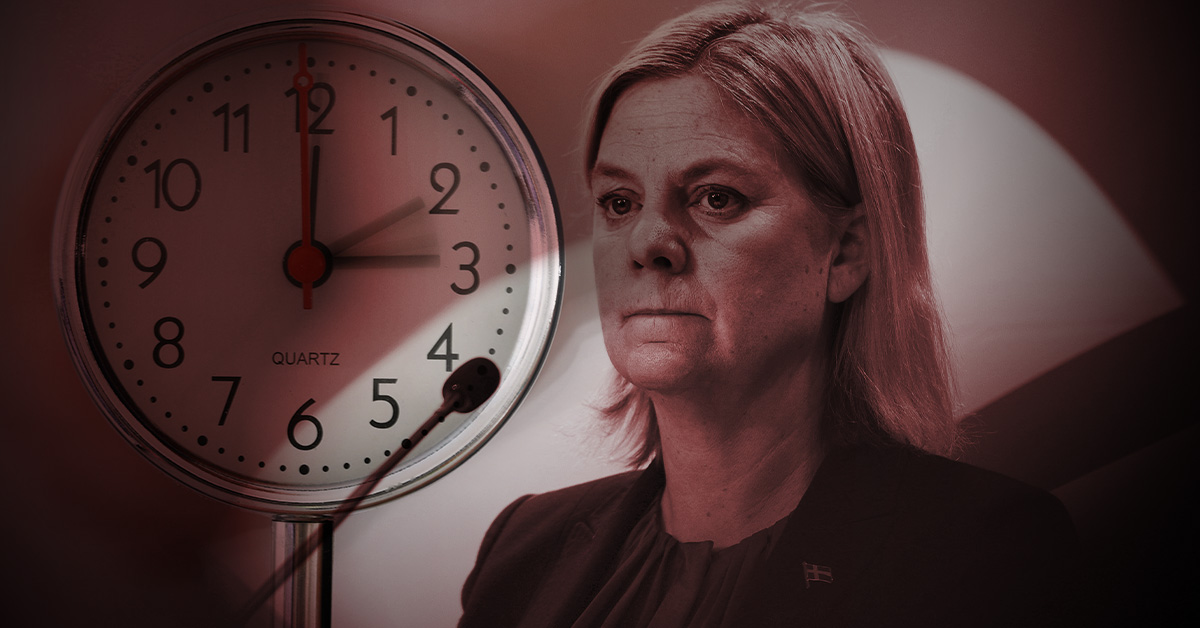 Magdalena Andersson iklädd kostym står bredvid en klocka som visar 11:00. Bilden har en mörk bakgrund.