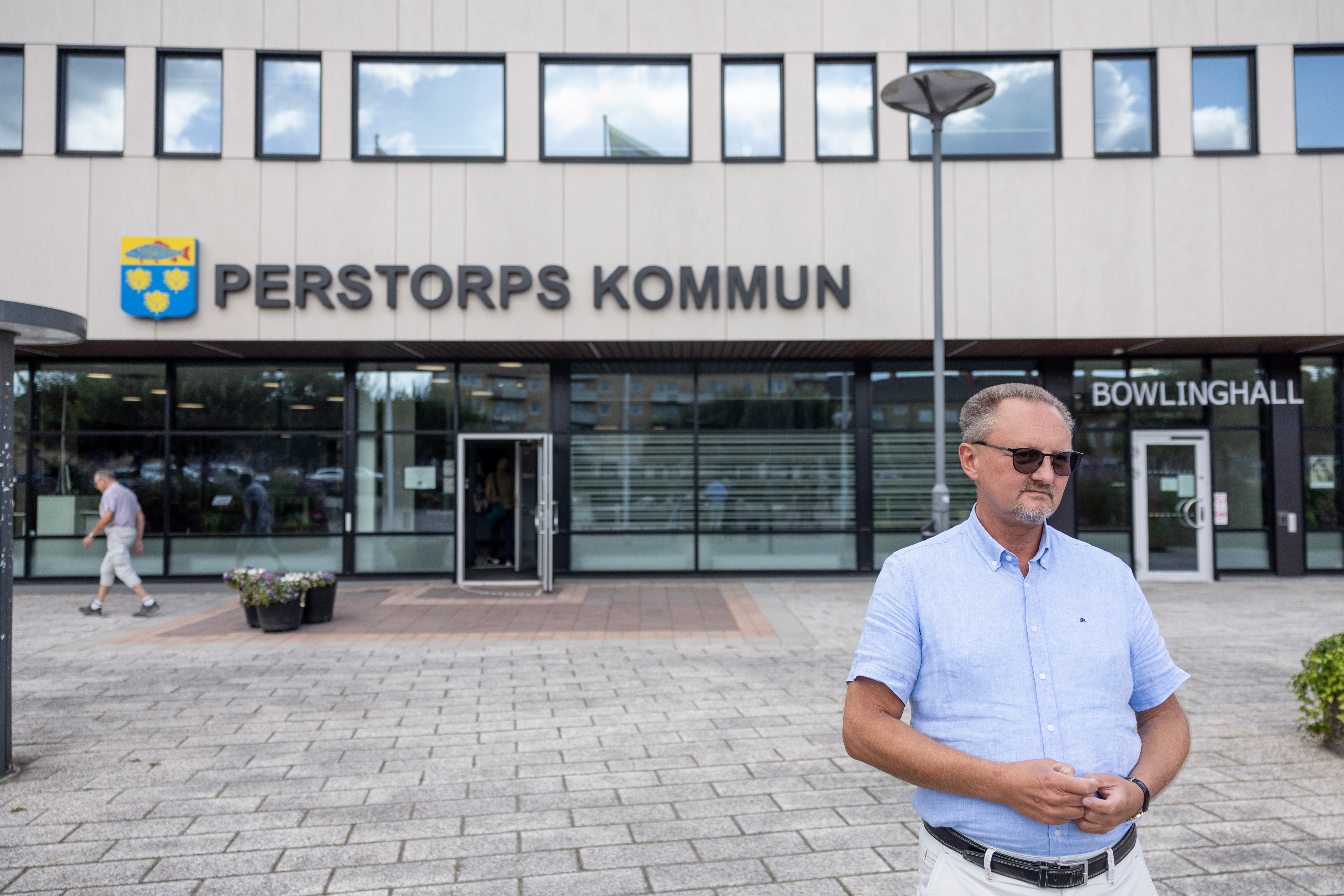 En man i blå skjorta står utanför Perstorps Kommuns byggnad. En annan person går in i byggnaden och en skylt med texten "Bowlinghall" syns.
