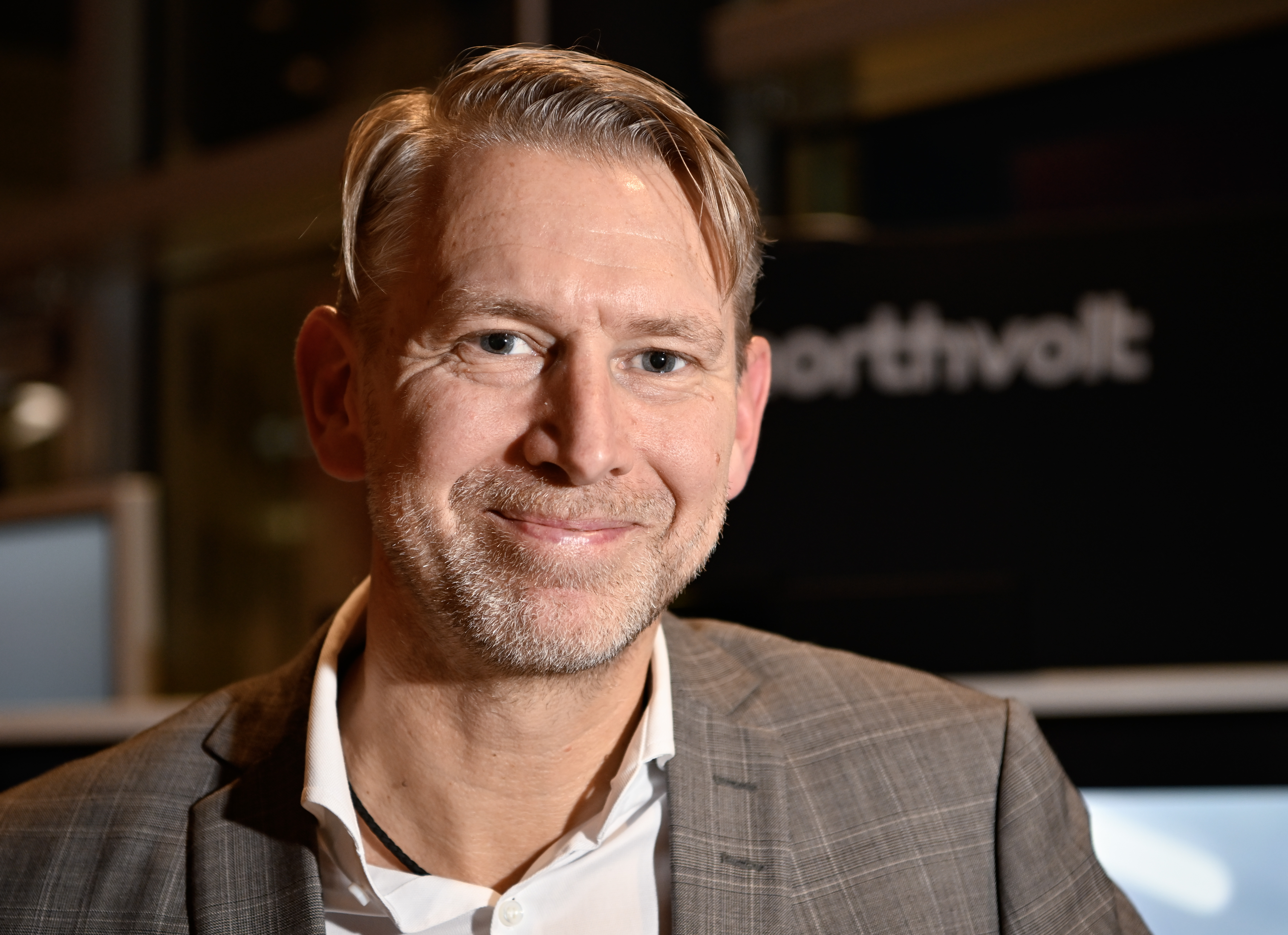 Peter Carlsson med kort, ljust hår och ett grått skägg. Han har på sig en grårutig kavaj och en vit skjorta. Bakgrunden är något oskarp och visar del av en "Northvolt"-skylt.