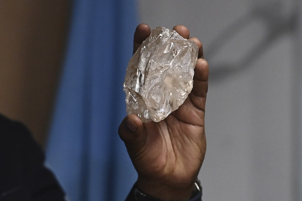En hand håller i en stor diamant, mot en suddig bakgrund.