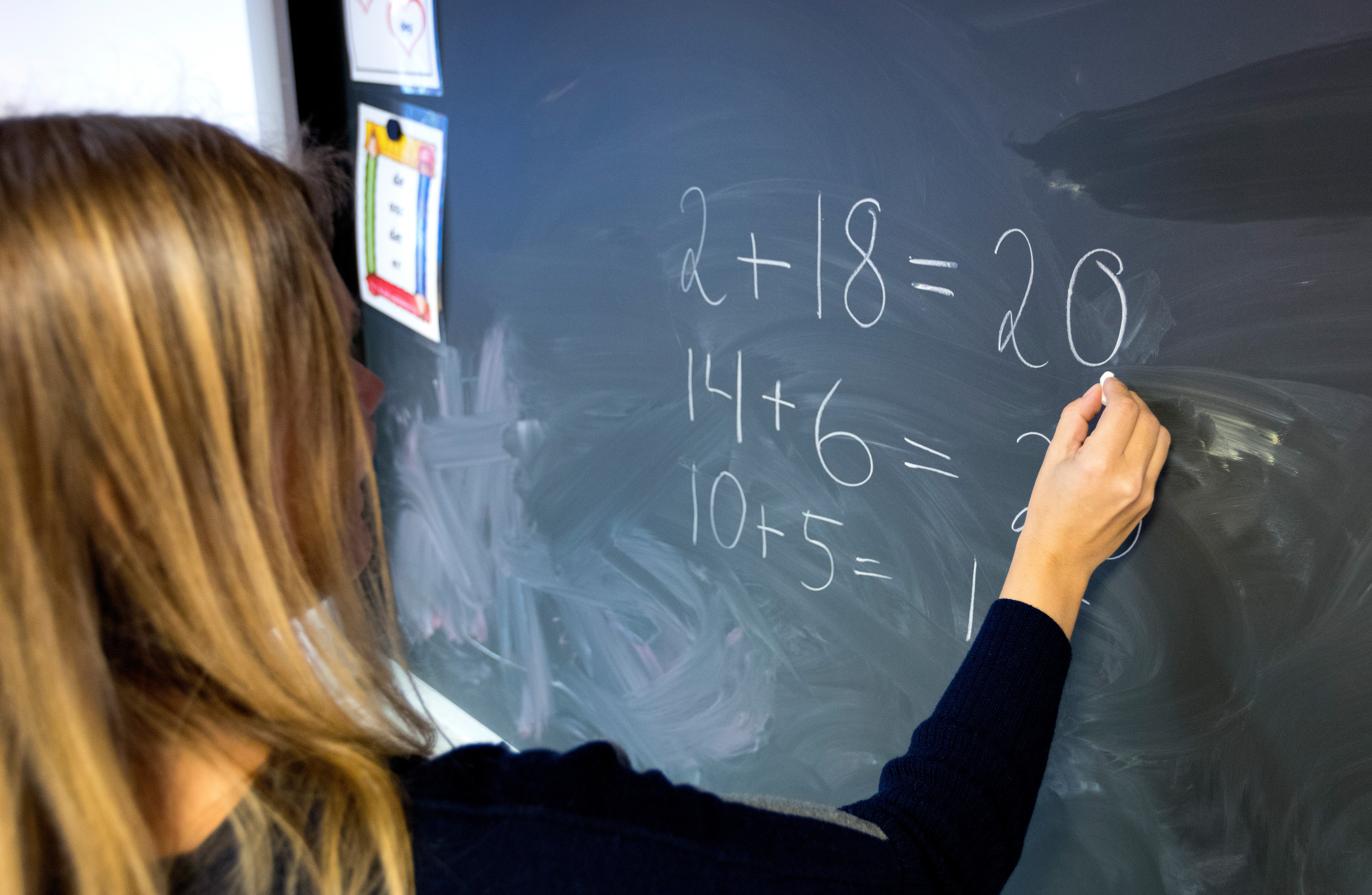 En person med långt hår skriver matematiska ekvationer på en svart tavla.