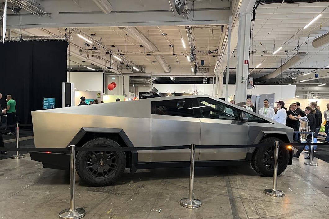 En silverfärgad, kantig eldriven lastbil visa inomhus omgiven av avspärrningar. Personer står i bakgrunden och tittar på lastbilen.