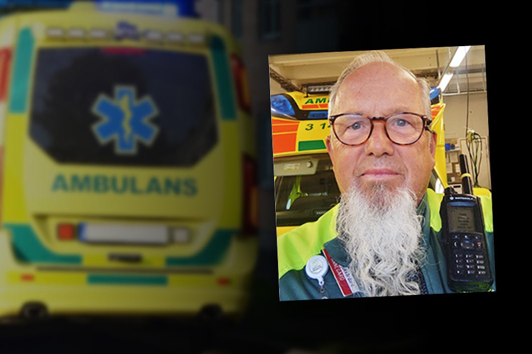 En man med långt vitt skägg och glasögon, klädd i grön och gul uniform, står framför en ambulans där det står "AMBULANS.