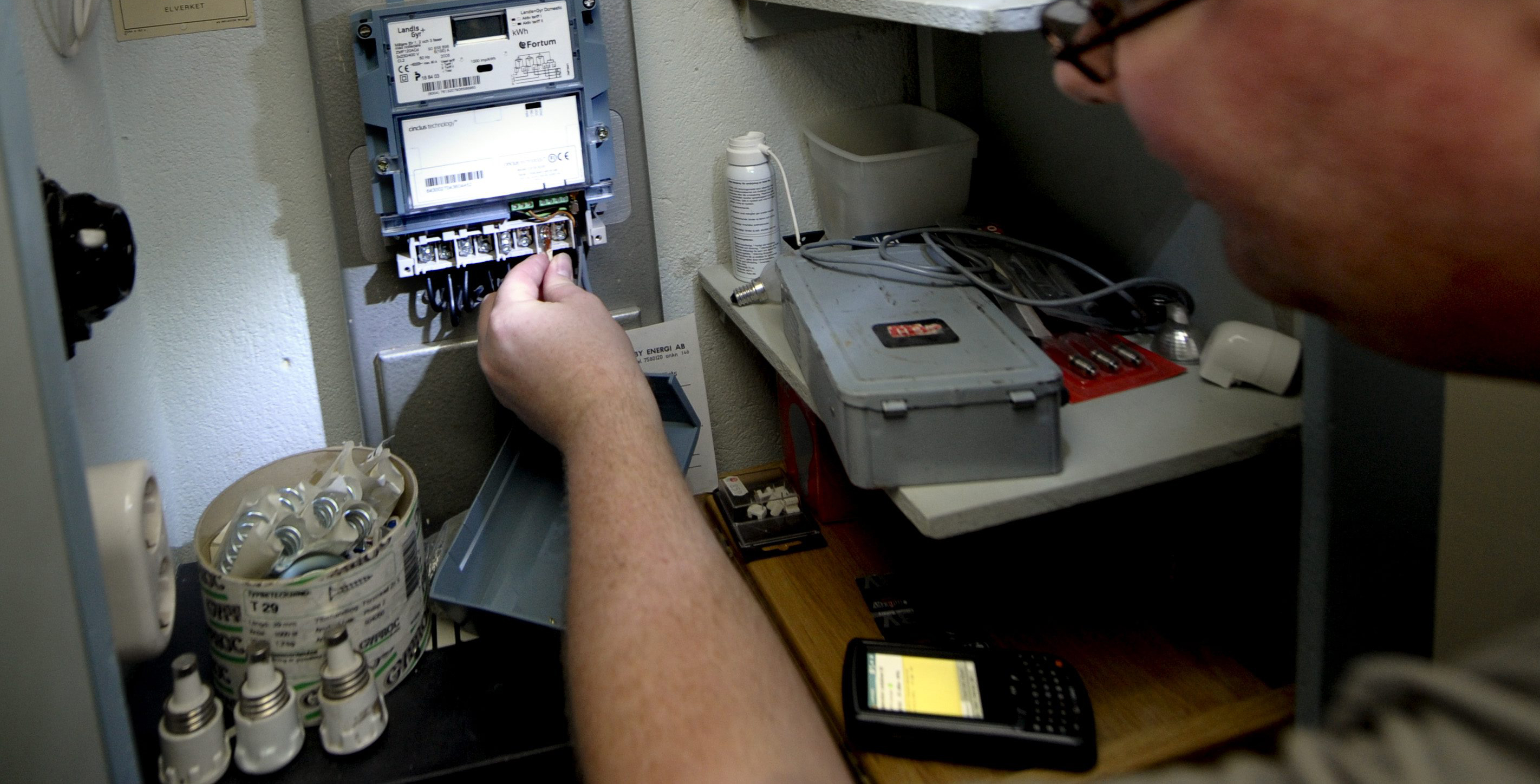 En person arbetar på en elmätarlåda med verktyg och utrustning i närheten.